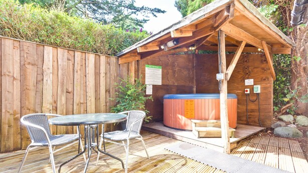 A wooden hot tub area with a table and chairs, surrounded by a wooden fence and vegetation. - Sleeps 12 guests in 6 bedrooms with 2 hot tubs (Coniston)