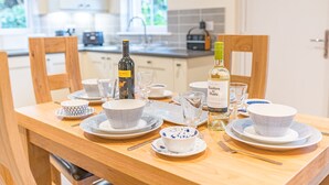Een eettafel gedekt met borden, kommen, glazen en flessen, met een keuken op de achtergrond.