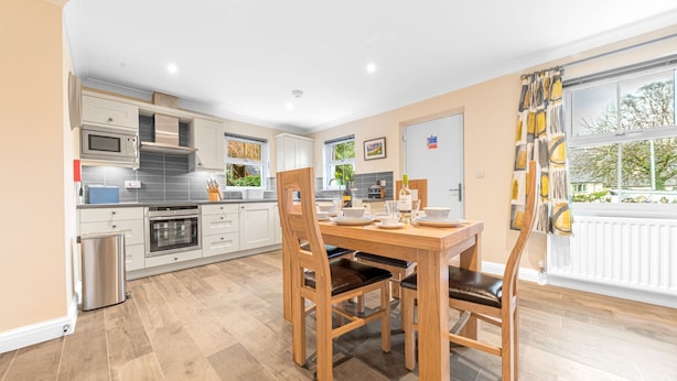 Een moderne keuken met witte kastjes, een roestvrijstalen oven en een eethoek met een houten tafel en stoelen.