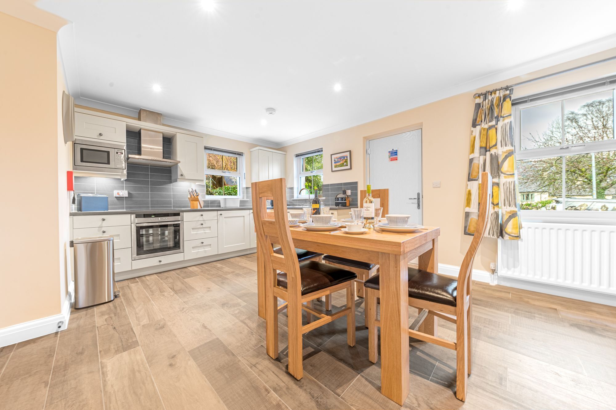 Een moderne keuken met witte kastjes, een roestvrijstalen oven en een eethoek met een houten tafel en stoelen.
