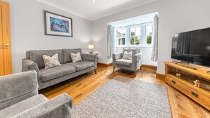 Un salon avec un canapé gris, une table basse en bois, un téléviseur et une fenêtre avec des rideaux.