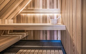 A sauna with wooden walls and benches, a bench with a bucket, and a black floor.
