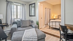 Ein modernes Schlafzimmer mit grauem Sofa, einem kleinen Tisch, einem Bett mit Kopfteil und einem Spiegel an der Wand.
