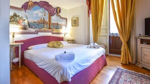 A hotel room with a large bed, a painting of a cityscape, a television, and a wooden floor.