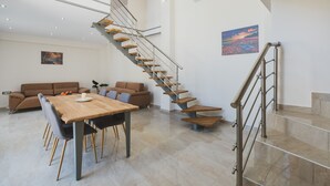 Un espace de vie moderne avec une table à manger en bois, un canapé marron, un escalier avec des rampes en métal et un tableau accroché au mur.