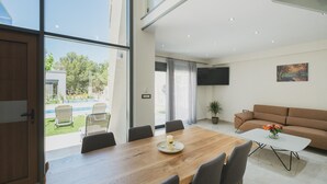 Un salon moderne avec une table à manger en bois, des chaises grises, un canapé marron et un téléviseur fixé au mur.