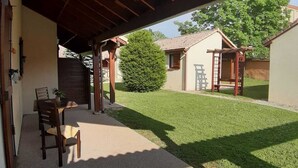 Un patio techado con una mesa y sillas, un pequeño jardín y un edificio al fondo.