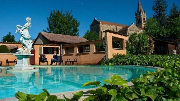 Una piscina con una estatua, una iglesia y un edificio con tejado de azulejos.