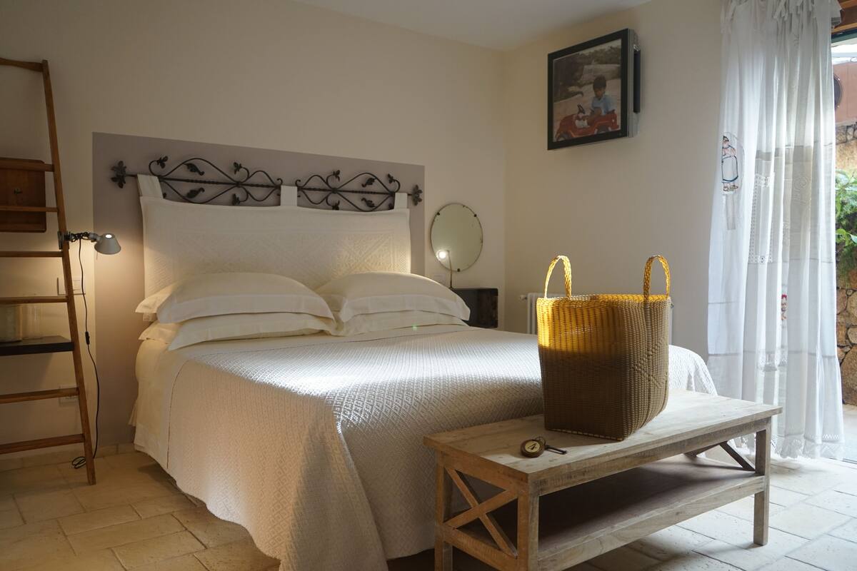 Een slaapkamer met een bed, een nachtkastje met een mand, een spiegel aan de muur en een ladder.