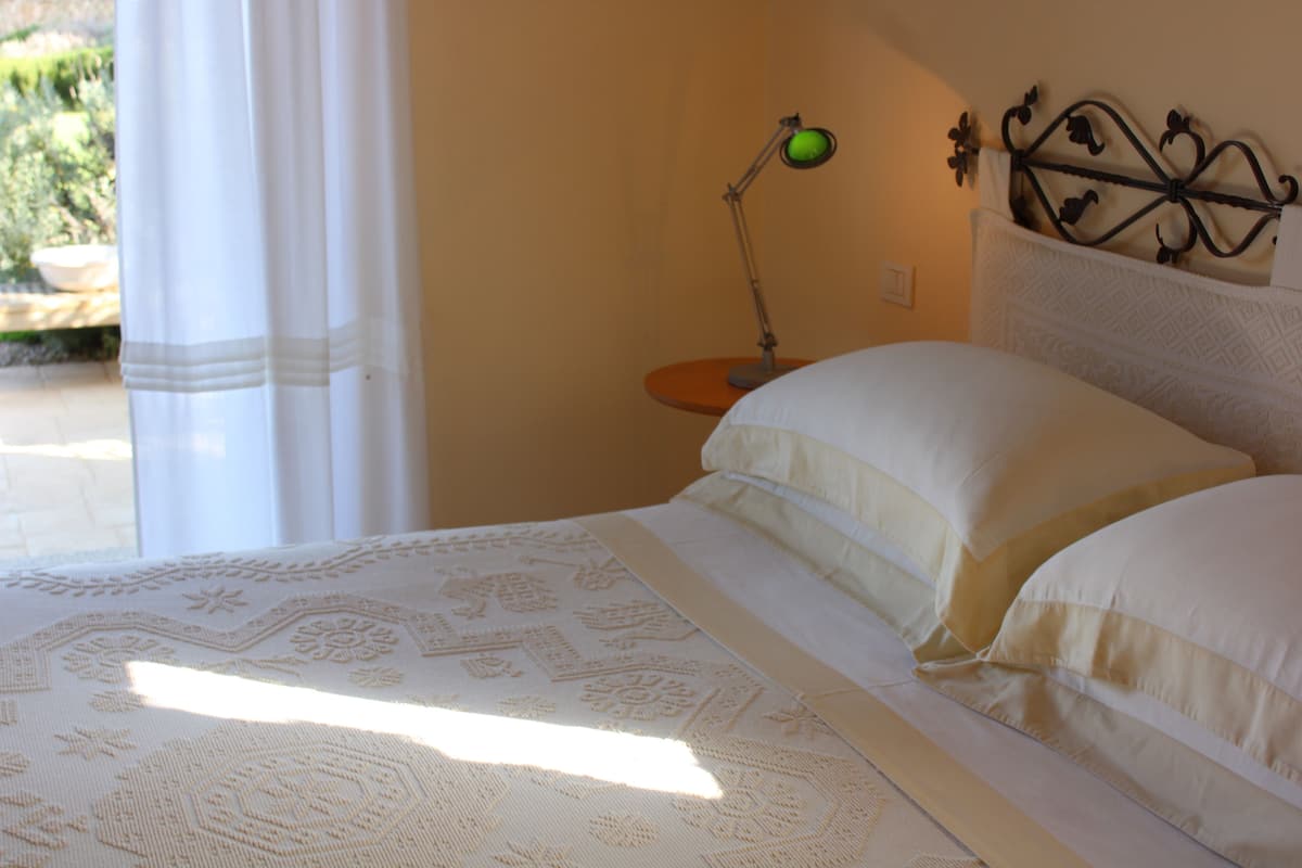 Een bed met beddengoed met patroon, een nachtkastje met lamp en een raam met gordijnen.