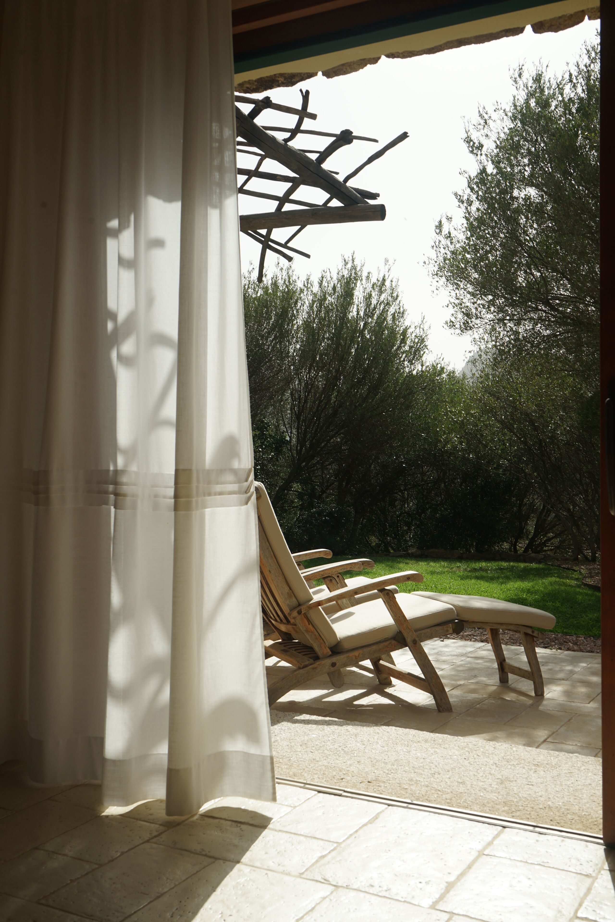 Un espacio al aire libre cubierto con una pérgola, dos sillones de descanso y vista a un jardín.