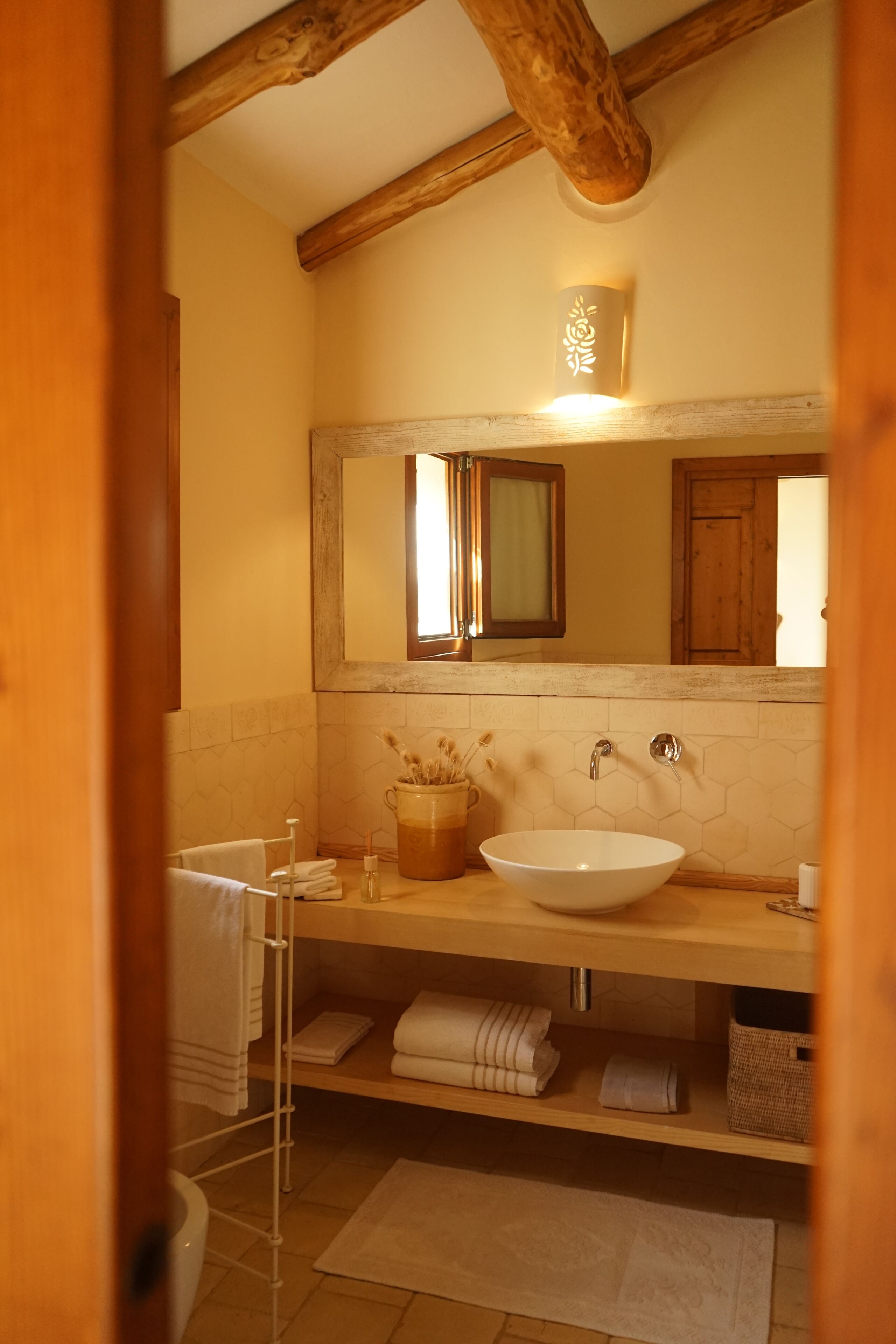 Un baño con techo de madera, un espejo grande, un lavamanos blanco y un perchero para toallas.