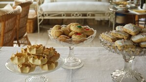 Een tafel met verschillende gebakjes en een witte tafelkleed met geborduurde tekst.