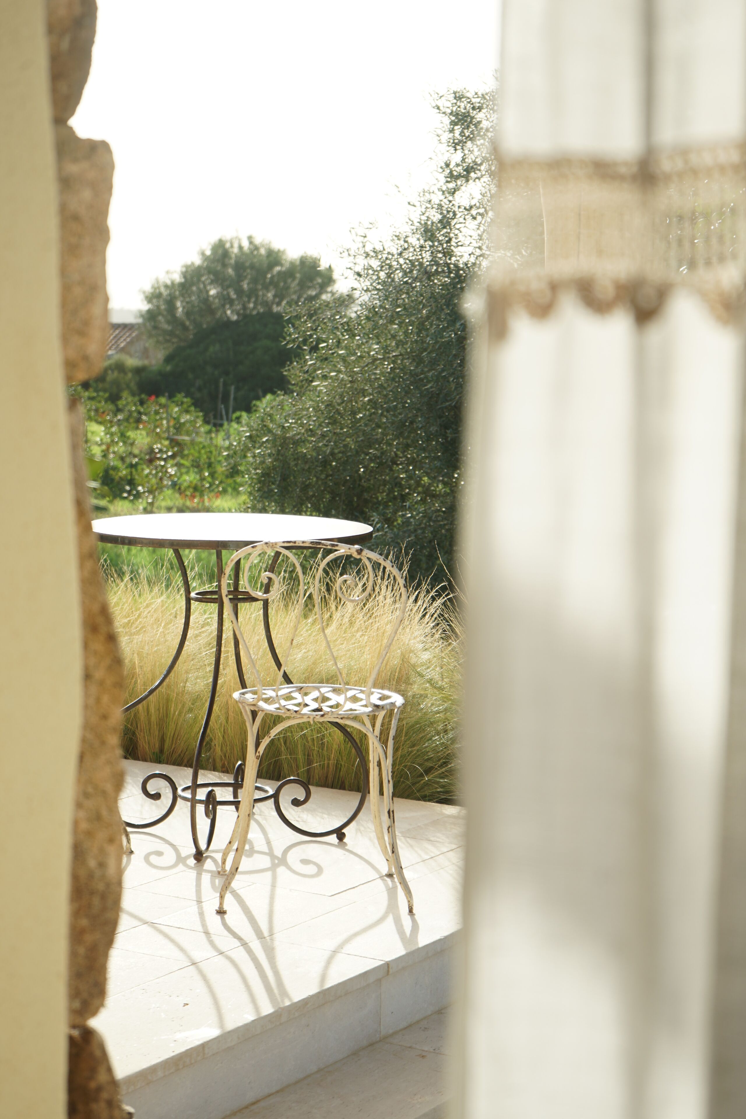 Een terras met een ronde tafel en twee stoelen, omgeven door groen en een stenen muur.