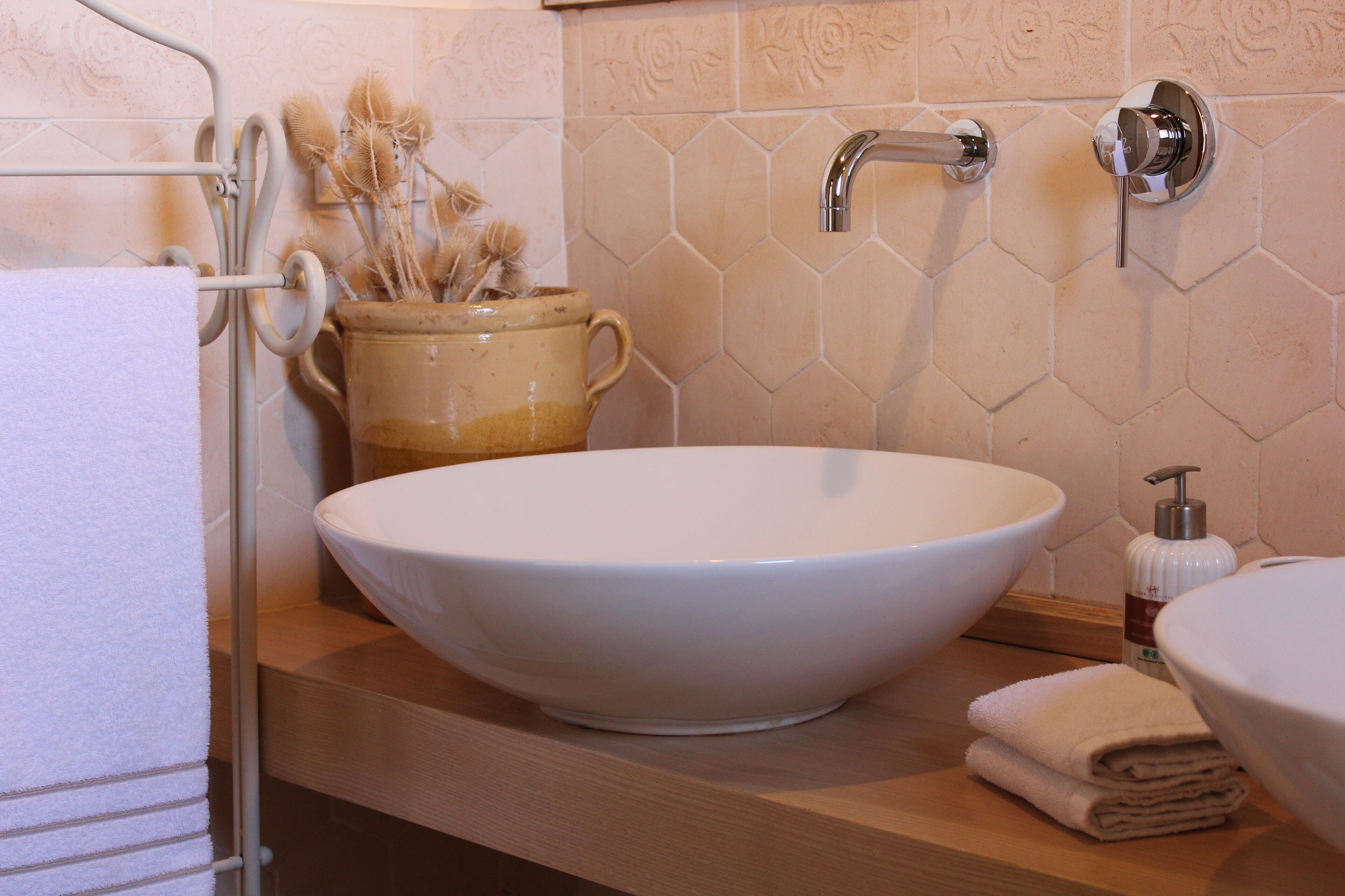 A bathroom with a large white vessel sink, a handheld showerhead, and a towel rack with a towel.