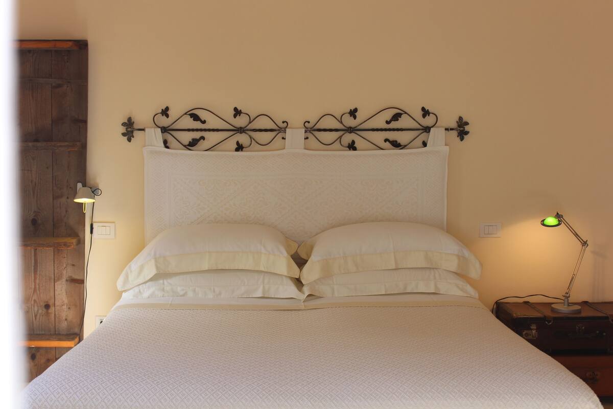 Een bed met een metalen hoofdeinde, een bedlampje en een houten deur op de achtergrond.
