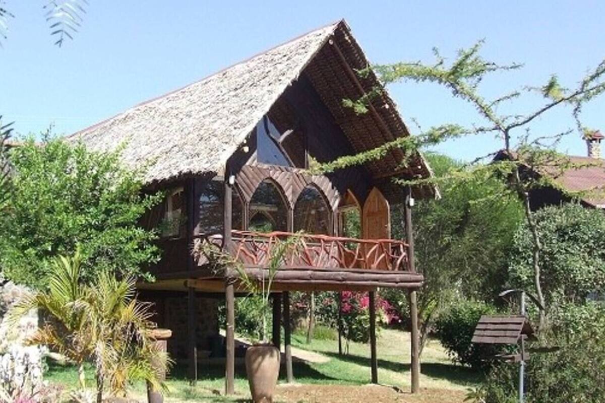 A traditional wooden house with a thatched roof, a balcony, and a garden with various plants.