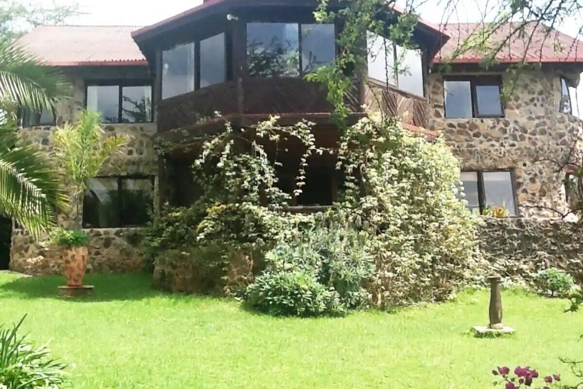 A two-story stone building with a red roof, surrounded by lush greenery and a well-maintained lawn.