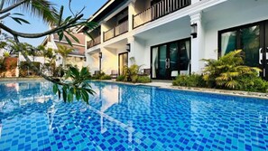 A swimming pool with a tiled edge, surrounded by a white building with balconies and large windows. - Manyo Hotel and Resort (Luang Prabang)