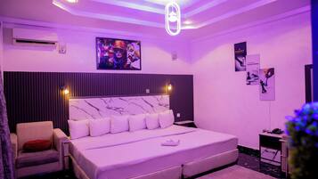 A modern bedroom with a large bed, a chair, a desk, and a wall-mounted air conditioner.