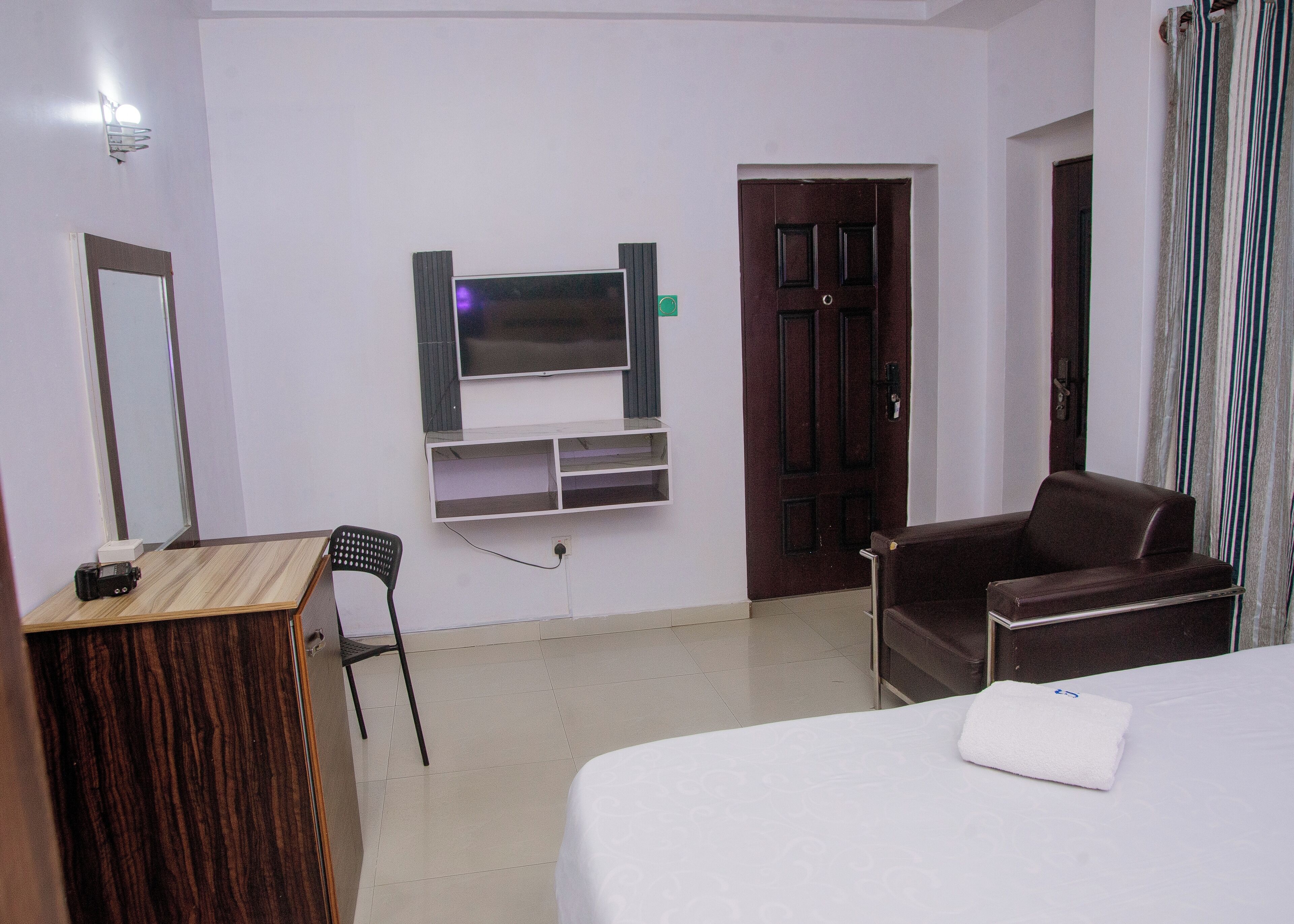 A hotel room with a bed, a desk, a chair, a television mounted on the wall, and a door.