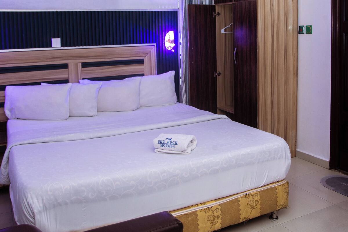 A hotel room with a large bed, a wardrobe, and a headboard with built-in speakers.