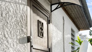 A white building with a textured exterior, a dark metal door with a decorative panel, and a small step leading to the entrance. - Breezy beach apt, steps to the sand! Full AC + Generator (Santurce)