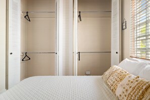 Un dormitorio con cama, armario con barra para colgar y ventana con persianas.