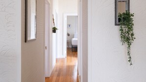 A hallway with white walls and wooden flooring, leading to a bedroom with a bed and a nightstand. - Breezy beach apt, steps to the sand! Full AC + Generator (Santurce)