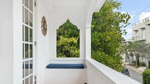 A balcony with a white wall, a window with a decorative arch, and a blue bench. - Breezy beach apt, steps to the sand! Full AC + Generator (Santurce)