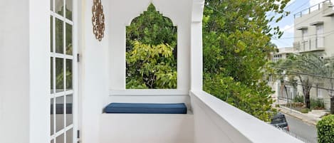 Un balcón con una pared blanca, una ventana con arco decorativo y un banco azul.