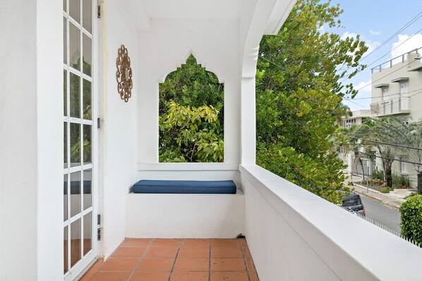 A balcony with a white wall, a window with a decorative arch, and a blue bench.