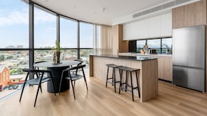 A modern kitchen with a large island, bar stools, and a stainless steel refrigerator. - Urban Rest Parramatta Apartments (Harris Park)