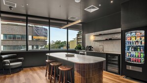 A modern kitchen with a central island, bar stools, a built-in refrigerator, and a large window offering a view of the city. - Urban Rest Parramatta Apartments (Harris Park)