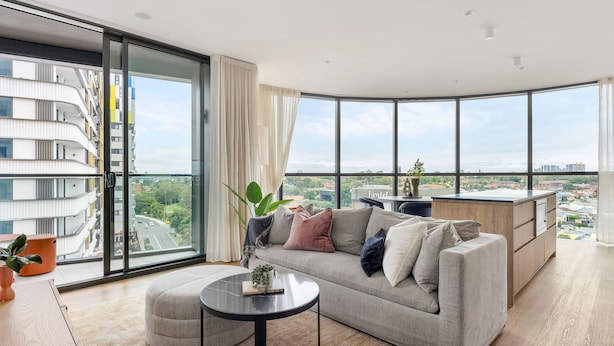 A modern living room with a large window, a sofa, a coffee table, and a kitchen area. - Urban Rest Parramatta Apartments (Harris Park)