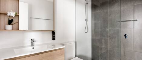 A modern bathroom with a wooden vanity, white sink, and a shower with a glass door.