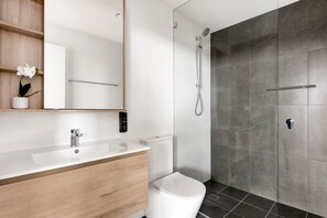 A modern bathroom with a wooden vanity, white sink, and a shower with a glass door. - Urban Rest Parramatta Apartments (Harris Park)