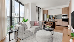 A modern apartment with a large window, a sofa, a dining table, and a kitchen area. - Urban Rest Parramatta Apartments (Harris Park)