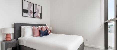 A modern hotel room with a large bed, a nightstand with a lamp, and abstract wall art.