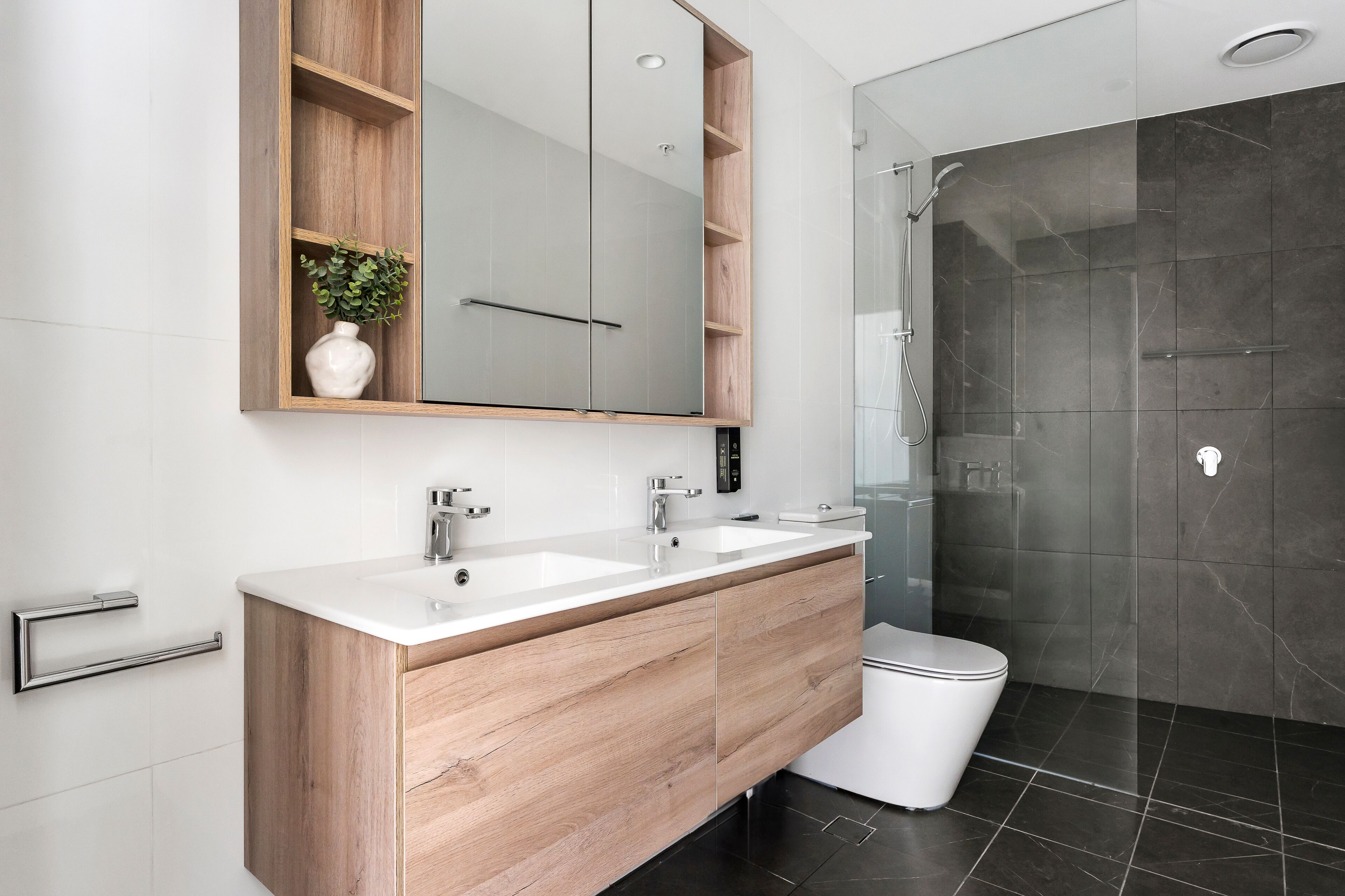 A modern bathroom with a wooden vanity, two sinks, a large mirror, and a walk-in shower.