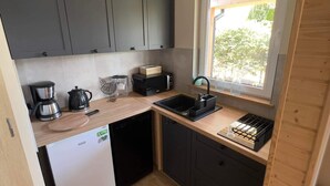 Uma cozinha compacta com armários cinza, lava-louças, cafeteira e janela com vista para o verde.