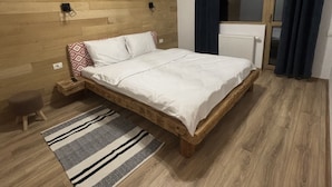 Ein Schlafzimmer mit Holzboden, einem Bett mit weißer Bettwäsche, einem gemusterten Teppich und einem Fenster mit Vorhängen.