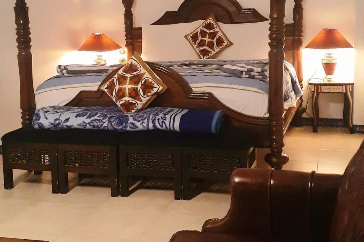 A four-poster bed with a canopy, two bedside tables with lamps, a framed picture on the wall, and a patterned rug on the floor.