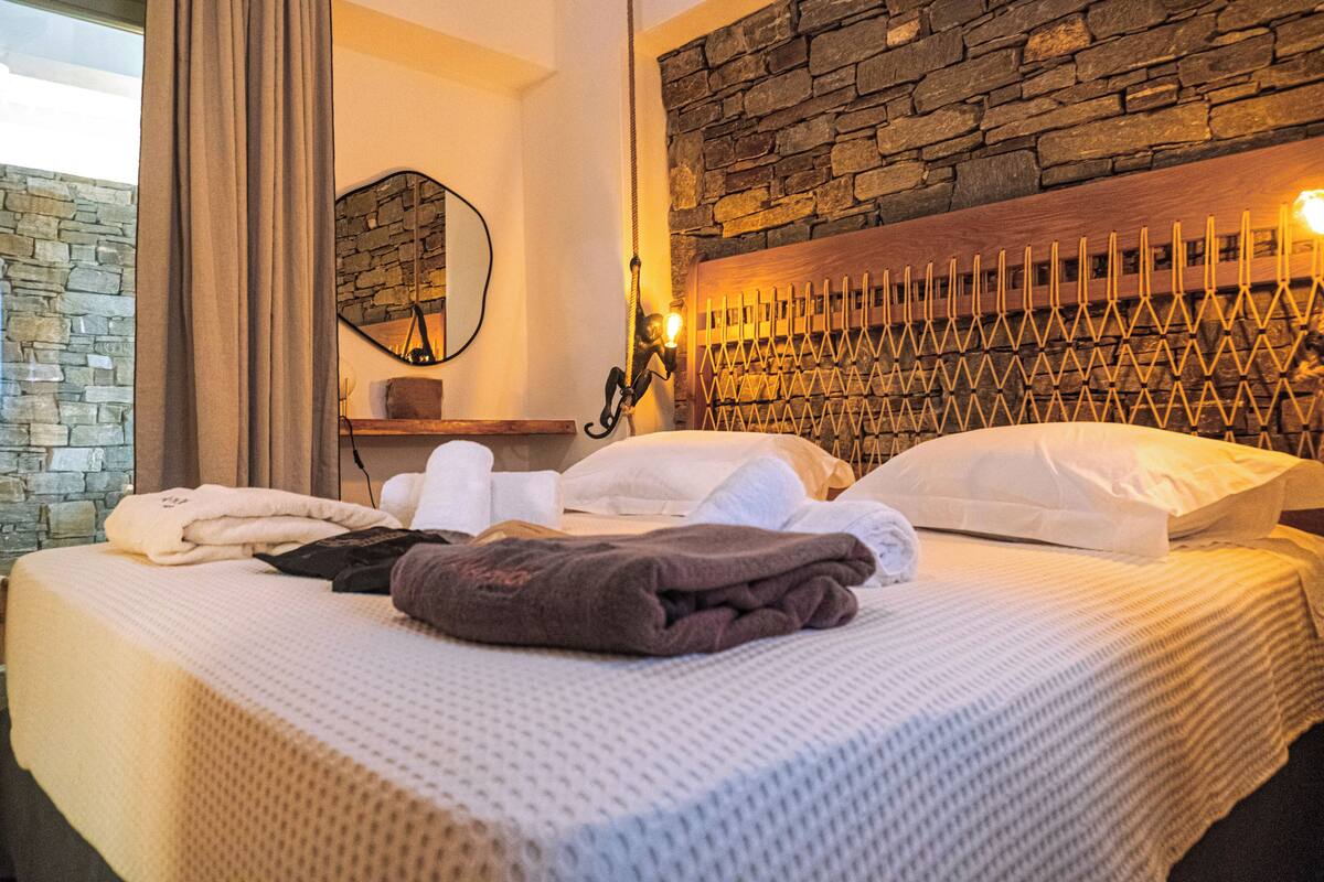 A neatly made bed with white and brown linens, a stone wall, and a wooden headboard with a unique design.