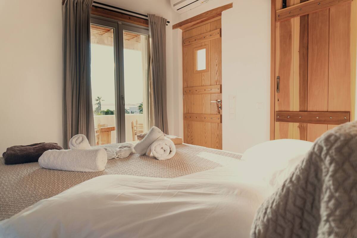 A hotel room with a bed, a wooden wardrobe, and a window with curtains.