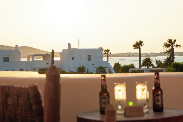 A table with bottles and candles, overlooking a coastal area with white buildings and palm trees.