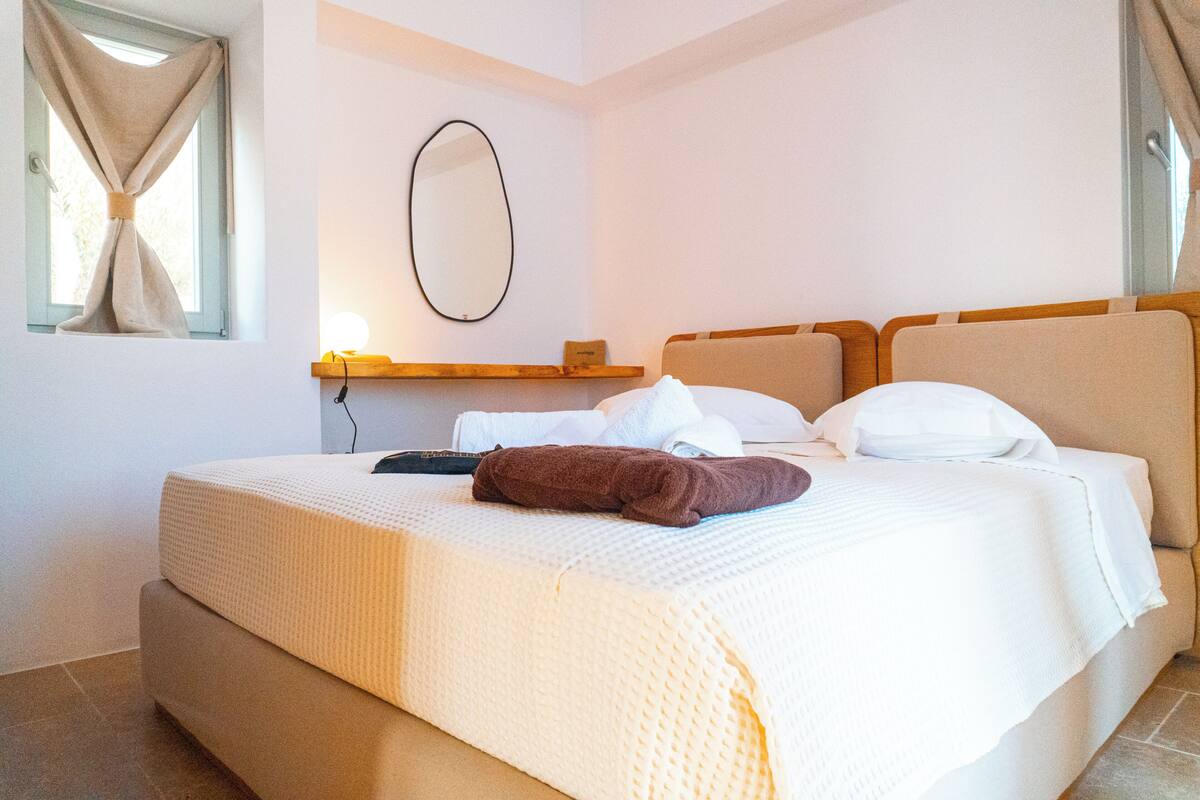 A neatly made bed with a white and beige duvet, a brown towel, and a bedside table with a lamp.