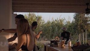 A group of people dining outdoors with a wooden table, surrounded by vegetation. - Anapnoe Resort by ParosKite (Paros)