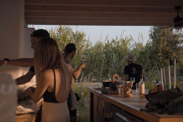 Un groupe de personnes est réuni autour d’une table en bois, à l’extérieur, et est entouré de verdure.