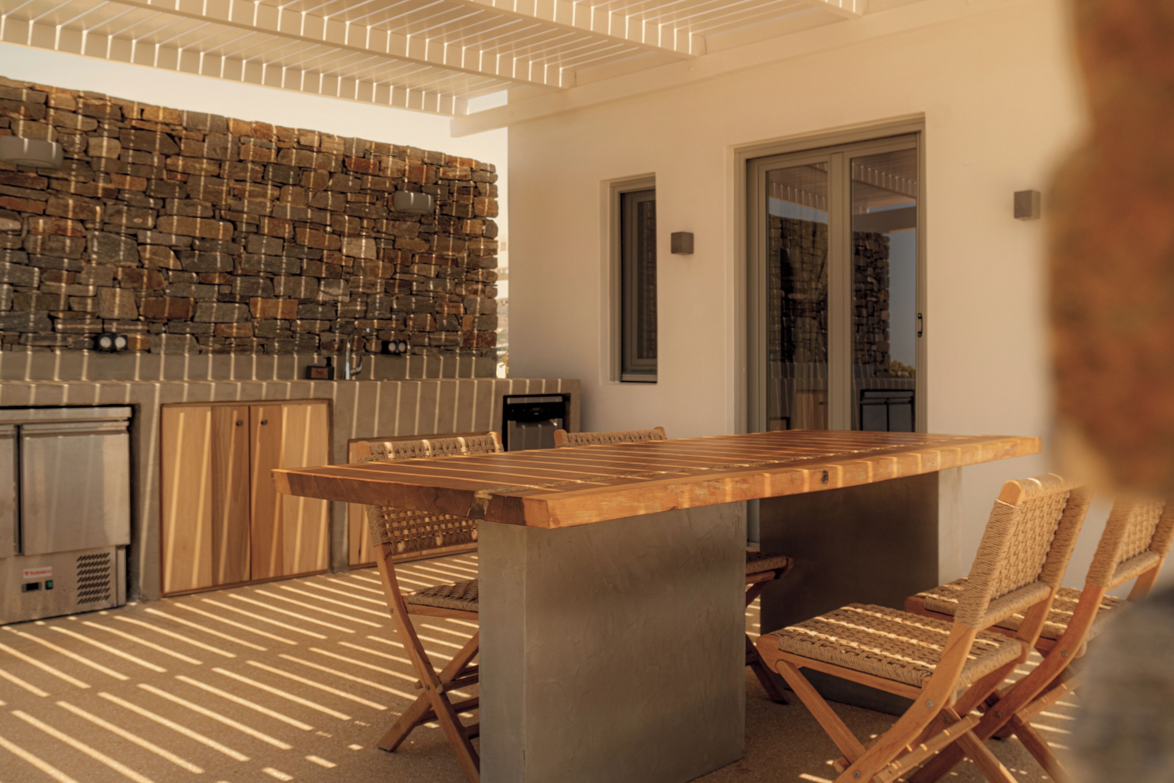 Een terras met een stenen muur, een houten tafel en rieten stoelen.
